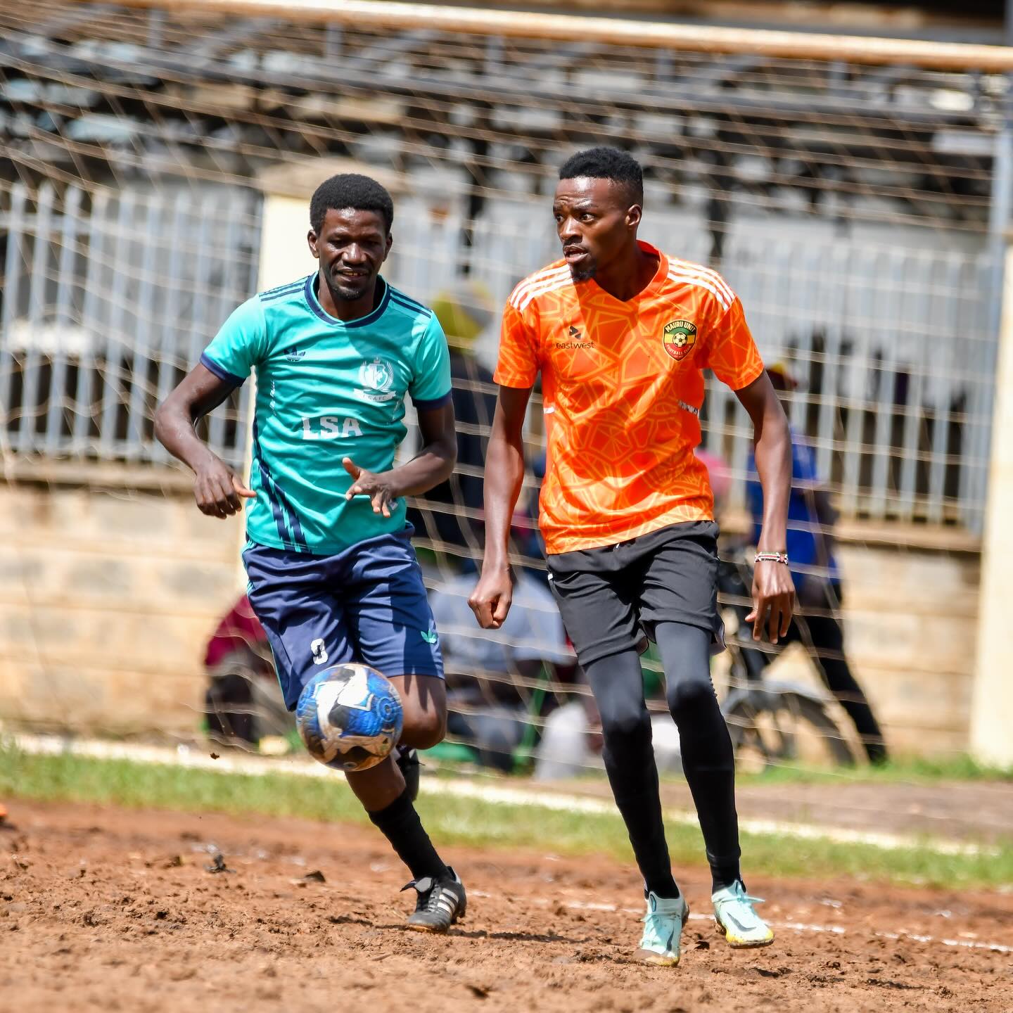 Two Nairobi West players chasing the ball across a dry pitch during a branch league match